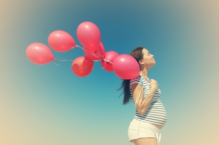 Young pregnant woman holding red balloons. Photo in old color image style.の写真素材