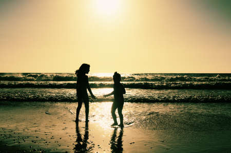 two happy kids playing on the beach at sunsetの写真素材