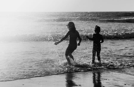 two happy kids playing on the beach at sunsetの写真素材