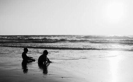 two happy kids playing on the beach at sunsetの写真素材