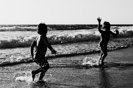 two happy kids playing on the beach at sunsetの写真素材