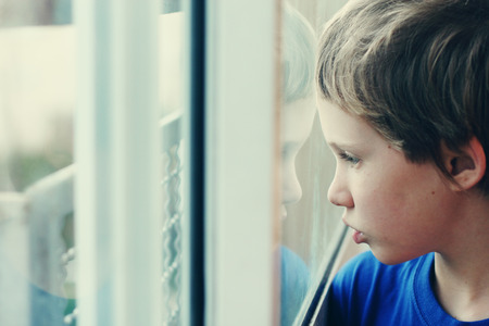 Cute 6 years old boy looking through the windowの写真素材