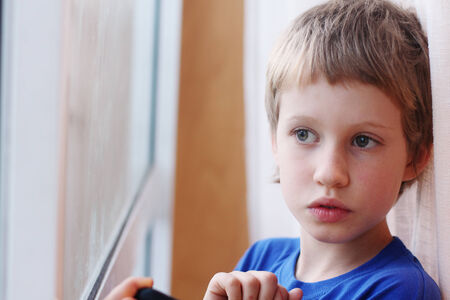 Cute 6 years old boy looking through the windowの写真素材