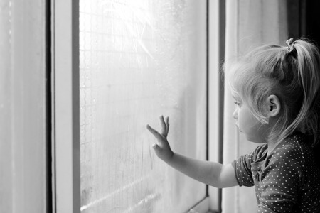 Cute 4 years old girl looking through the windowの写真素材