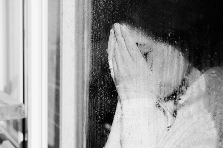 Art portrait of a beautiful young sadly girl looking through the windowの写真素材
