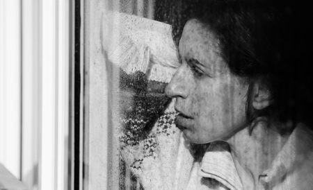 Art portrait of a beautiful young sadly girl looking through the windowの写真素材