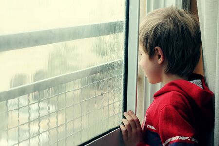 Cute 6 years old boy looking at the rainの写真素材