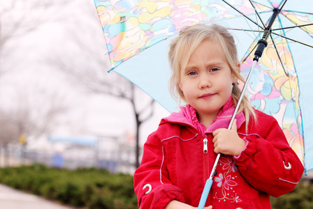adorable blonde girl holding colorful umbrella walking in the streetの写真素材