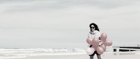 beautiful woman holding red balloons and walking on seasideの写真素材