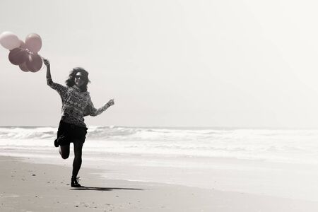 beautiful woman holding red balloons and walking on seasideの写真素材