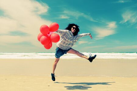 beautiful woman holding red balloons and walking on seasideの写真素材