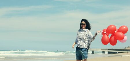 beautiful woman holding red balloons and walking on seasideの写真素材