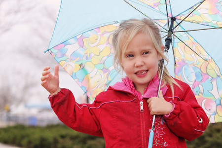 adorable blonde girl holding colorful umbrella walking in the streetの写真素材