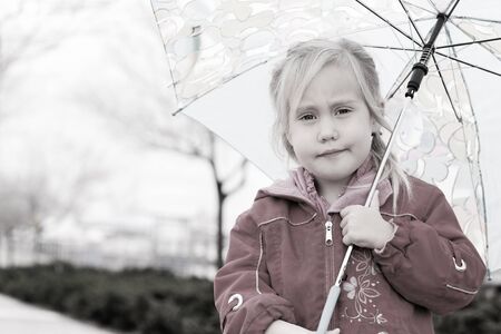 adorable blonde girl holding colorful umbrella walking in the streetの写真素材