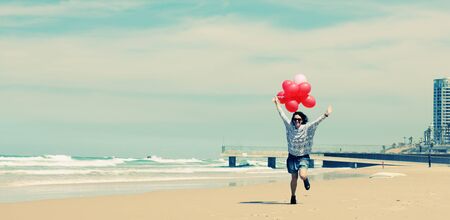 beautiful woman holding red balloons and walking on seasideの写真素材