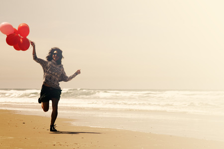 beautiful woman holding red balloons and walking on seasideの写真素材