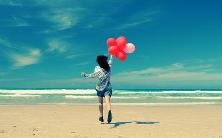 beautiful woman holding red balloons and walking on seasideの写真素材