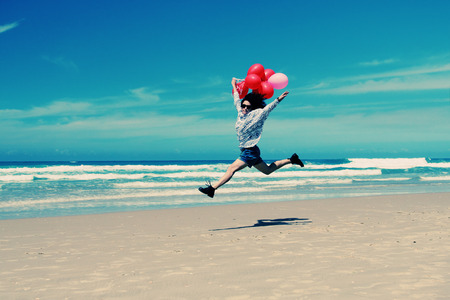 beautiful woman holding red balloons and walking on seasideの写真素材
