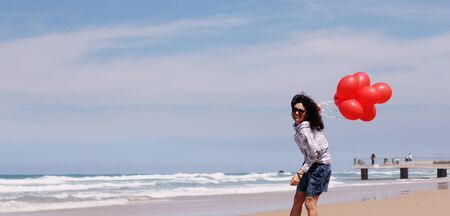 beautiful woman holding red balloons and walking on seaside