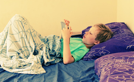 7 year old boy lies in bed and plays with a laptopの写真素材