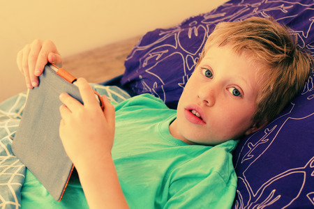 7 year old boy lies in bed and plays with a laptopの写真素材