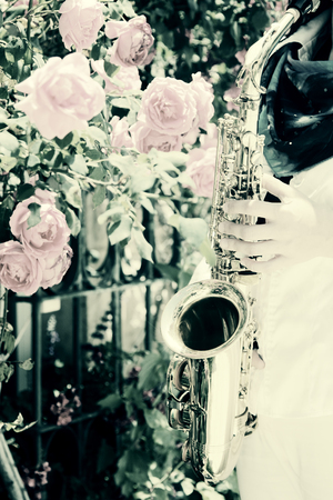 Saxophonist playing on saxophone on pink roses backgroundの写真素材