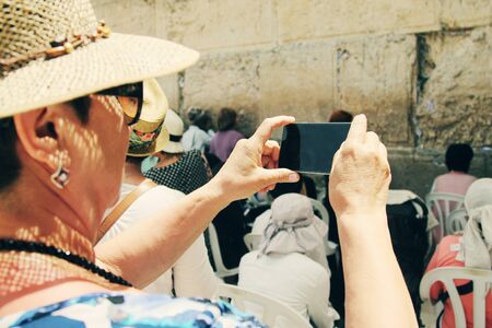 elderly woman takes a picture of the Western Wall and Jerusalem