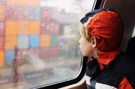 7 years old boy sitting in the train and looking to the rain
