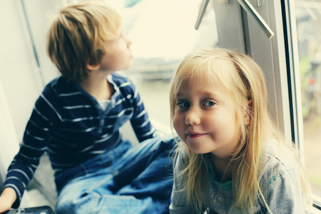 Sister and brother are sitting near the windowの写真素材