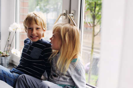 Sister and brother are sitting near the windowの写真素材