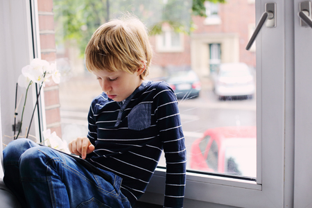 7 year old boy sitting near the window and playing tabletの写真素材