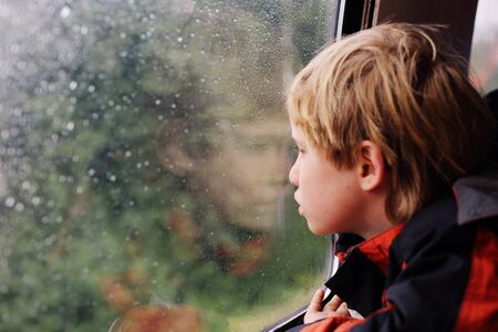 7 years old boy sitting in the train and looking to the rainの写真素材