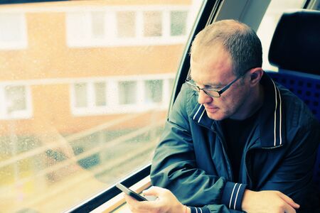 Handsome 40 years old man holding smartphone and traveling in the trainの写真素材