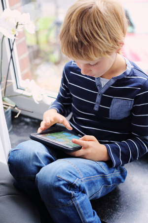 7 year old boy sitting near the window and playing tabletの写真素材