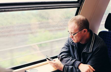 Handsome 40 years old man holding smartphone and traveling in the trainの写真素材