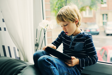 7 year old boy sitting near the window and playing tabletの写真素材
