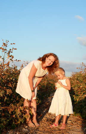 happy mother with daughter standing on a cotton field in sunset colorsの写真素材
