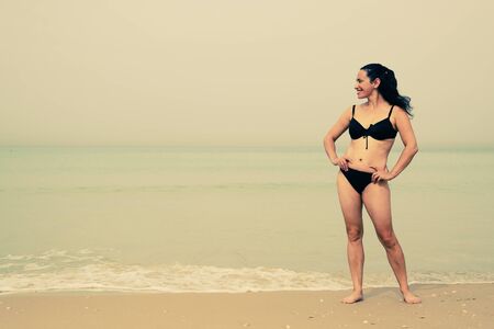 Beautiful woman standing on the beach with the sand, sea and blue sky in the backgroundの写真素材
