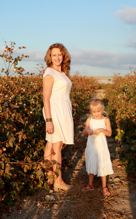happy mother with daughter standing on a cotton field in sunset colorsの写真素材