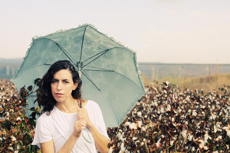 beautiful woman holding umbrella and standing in cotton fieldの写真素材