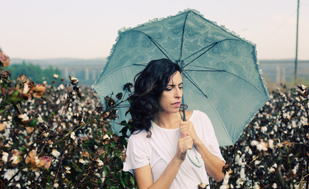 beautiful woman holding umbrella and standing in cotton fieldの写真素材