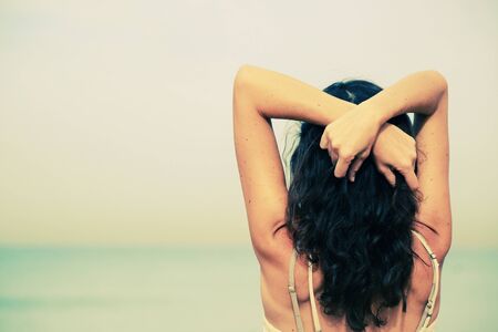 Beautiful woman standing on the beach with the sand, sea and blue sky in the backgroundの写真素材