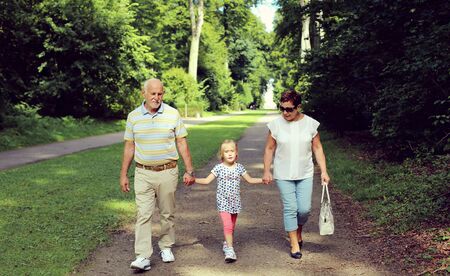 Grandparents With Grandchild walking together in the parkの写真素材