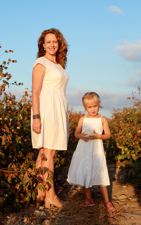 happy mother with daughter standing on a cotton field in sunset colorsの写真素材