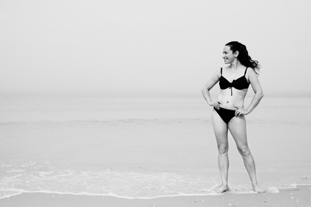 Beautiful woman standing on the beach with the sand, sea and blue sky in the backgroundの写真素材