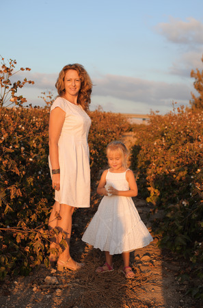 happy mother with daughter standing on a cotton field in sunset colorsの写真素材