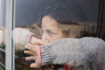beautiful 40 years old woman looking through the windowの写真素材