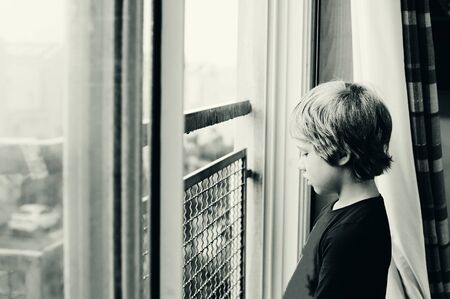 Cute 8 years old autustic boy looking at the rainの写真素材