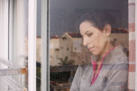 beautiful 40 years old woman looking through the windowの写真素材