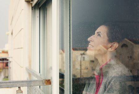 beautiful 40 years old woman looking through the windowの写真素材